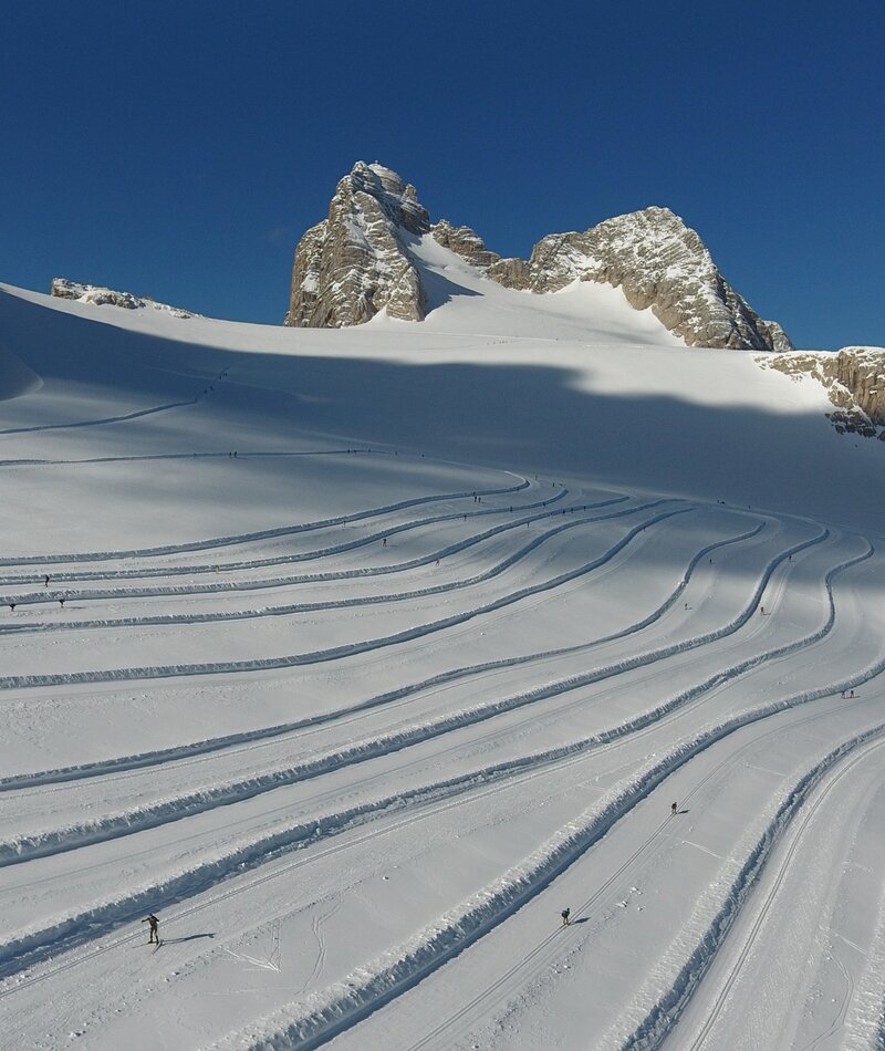 Snowy alpine slope with curving ski tracks and mountains | © photo-austria.at