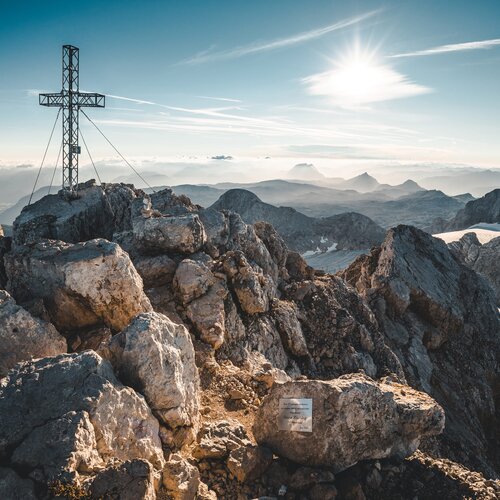 Metal cross atop rocky mountain summit with distant peaks