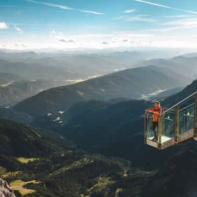 Person in orange jacket on glass viewing platform over mountains