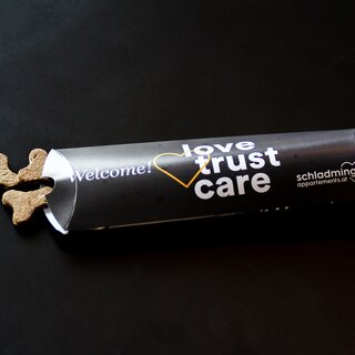 Rolled black banner with 'Welcome!' and 'love trust care' text; cookies nearby. | © SCHLADMING-APPARTEMENTS