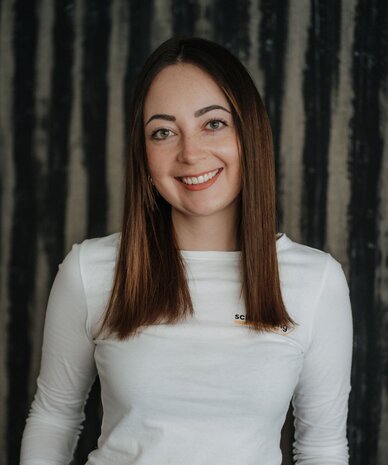 Smiling woman with long brown hair in white top and black belt