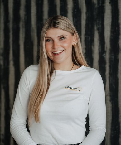 Smiling woman with long blonde hair in white shirt with 'schladming' logo