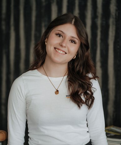 Smiling young woman standing indoors in a white top