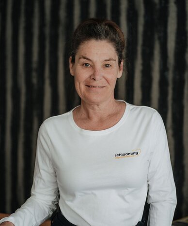 Woman wearing white shirt with schladming logo, standing by railing.