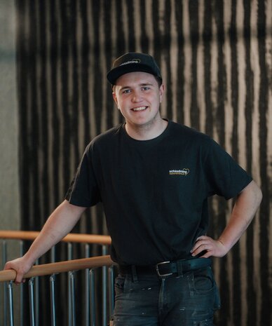 Young man in black t-shirt and cap leaning on railing indoors