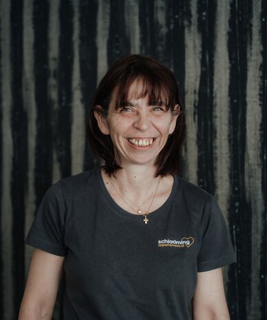 Smiling woman with brown hair in a dark T‑shirt against striped backdrop.