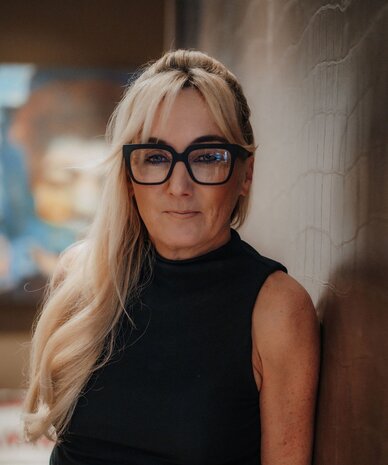 Woman with long blonde hair wearing black sleeveless top and glasses