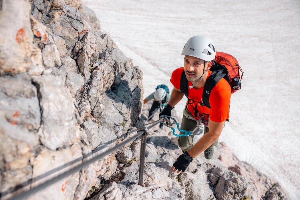 Two climbers ascend a rocky cliff with rope and gear.