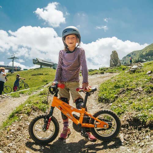 Child wearing helmet stands with orange bike on dirt trail