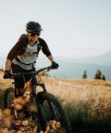 Mountain biker wearing helmet rides on a dirt trail with distant mountains