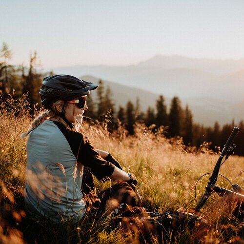 Cyclist wearing helmet sits in tall grass at sunset.