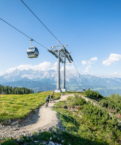 Cable car gondola over mountain landscape with cyclists | © Christoph Oberschneider