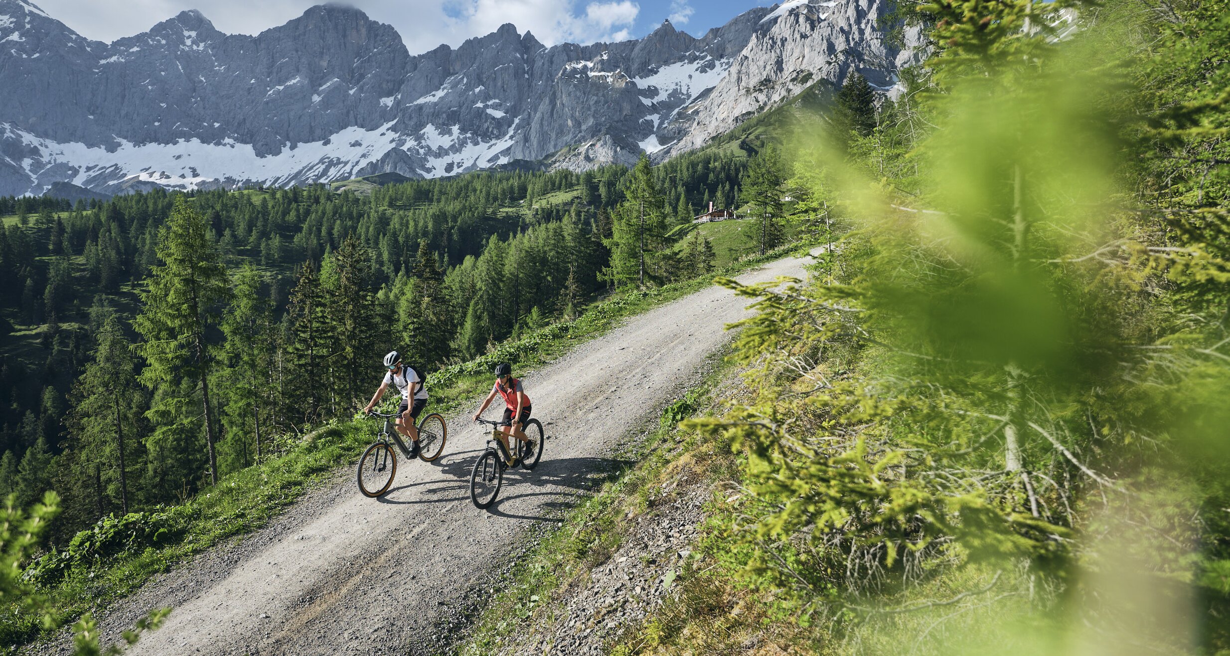 Two cyclists ride a dirt trail through a forested mountain landscape. | © RAPHAELGABAUER.COM