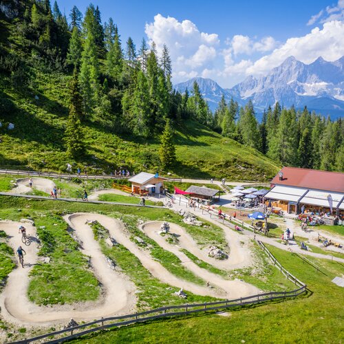 Mountain bikes ride on a winding dirt track beside a hillside cafe | © Christoph Oberschneider