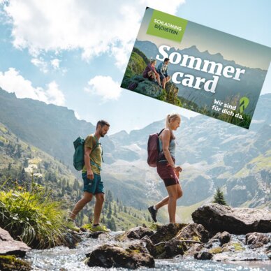 Hikers cross rocky stream beneath mountains; Sommer Card banner.