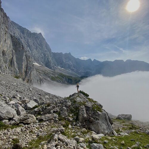 Person standing on rocky mountain ridge above clouds