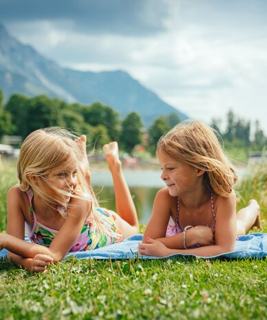 Two girls lying on a towel by a lake