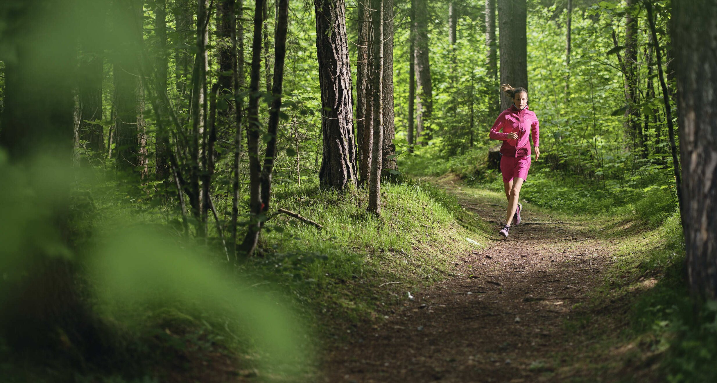 Female jogger in pink outfit running along forest trail | © RAPHAELGABAUER.COM