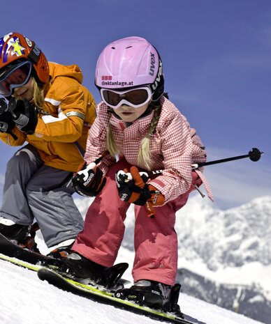 Two children with helmets and goggles snowboarding down a snowy slope | © Tom Lamm