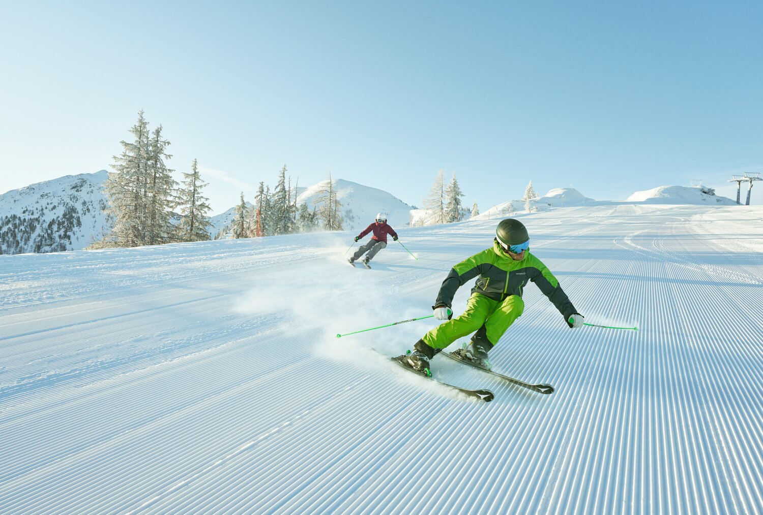 Two skiers carve turns on a groomed snowy slope