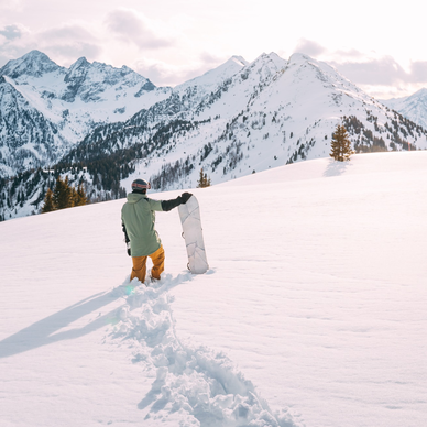 Snowboarder walking through deep snow toward distant snowy mountains