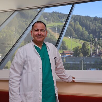 Medical professional in white coat by large glass windows with hillside view | © FotoTOM
