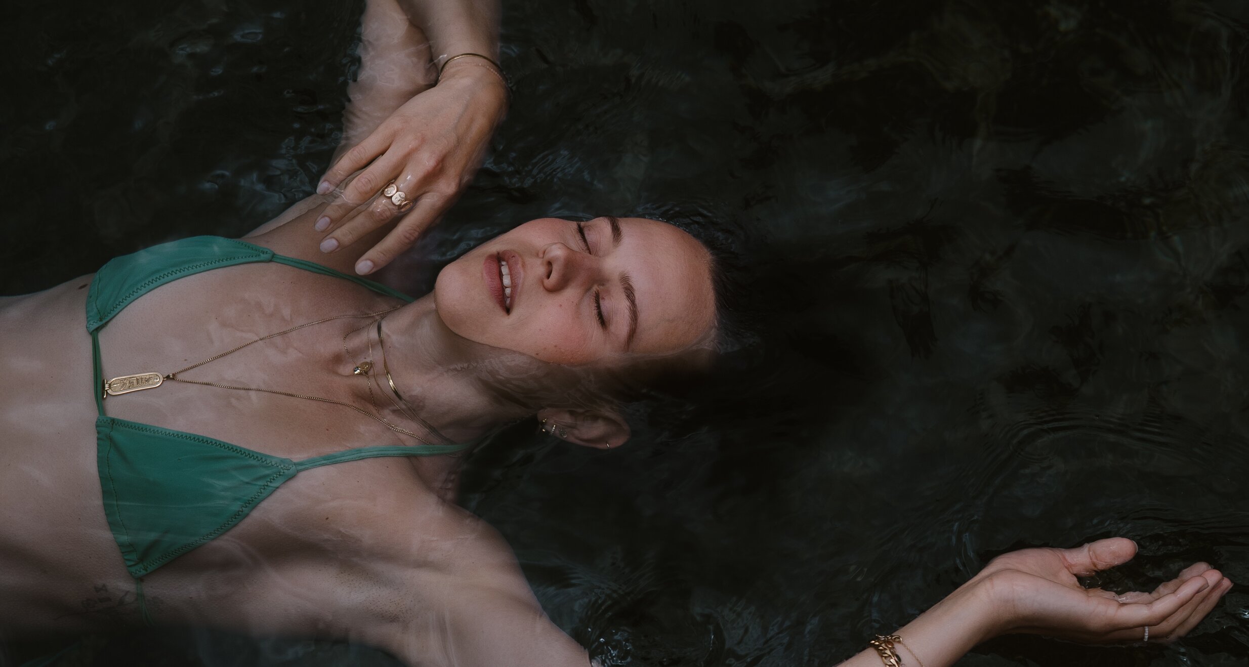 woman floating in dark water wearing a green bikini