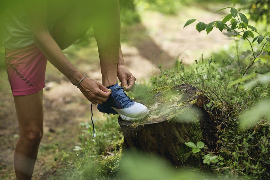 Person tying blue hiking shoe on a log in forest trail | © RAPHAELGABAUER.COM