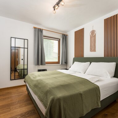 Double bed with green headboard and white pillows in modern bedroom.