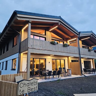 Two-story wooden chalet with balcony, outdoor seating at dusk.