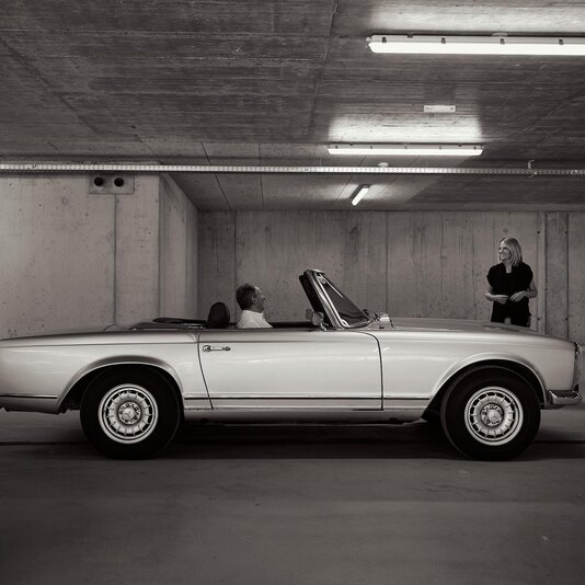 Classic silver convertible with two passengers inside in an underground garage. | © RaphaelGabauer