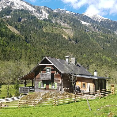 Wooden alpine cabin on a grassy meadow with snow-capped peaks