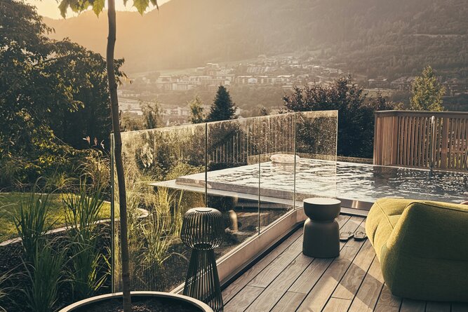 Sunlit wooden terrace with glass railing and distant mountains