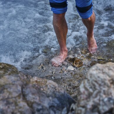 Person standing with blue shorts, feet in rocky water | © RAPHAELGABAUER.COM