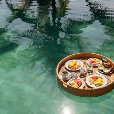 Wicker serving basket with breakfast plates floating on a pool