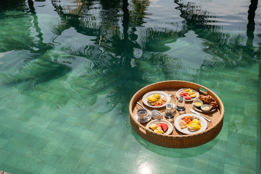Wicker serving basket with breakfast plates floating on a pool