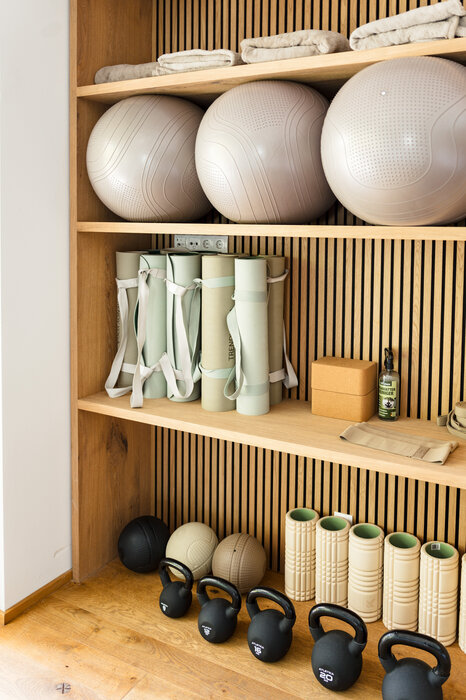 Wooden storage shelf holding gym balls, foam rollers, rolled mats, and kettlebells.
