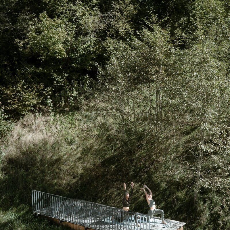 Two people practicing yoga on a raised platform in a forest clearing