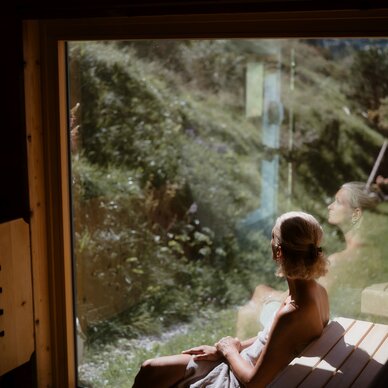 Woman wrapped in towel sits in sauna, gazing outside