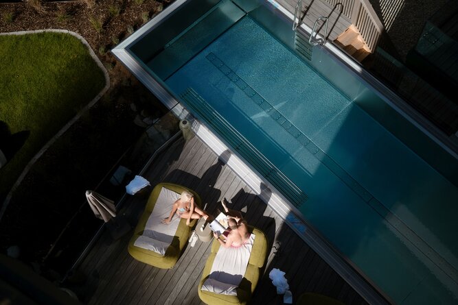 Two people relaxing on green lounge chairs beside a pool