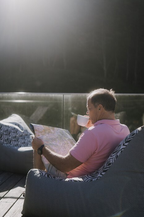Man in pink polo reads map on outdoor deck.