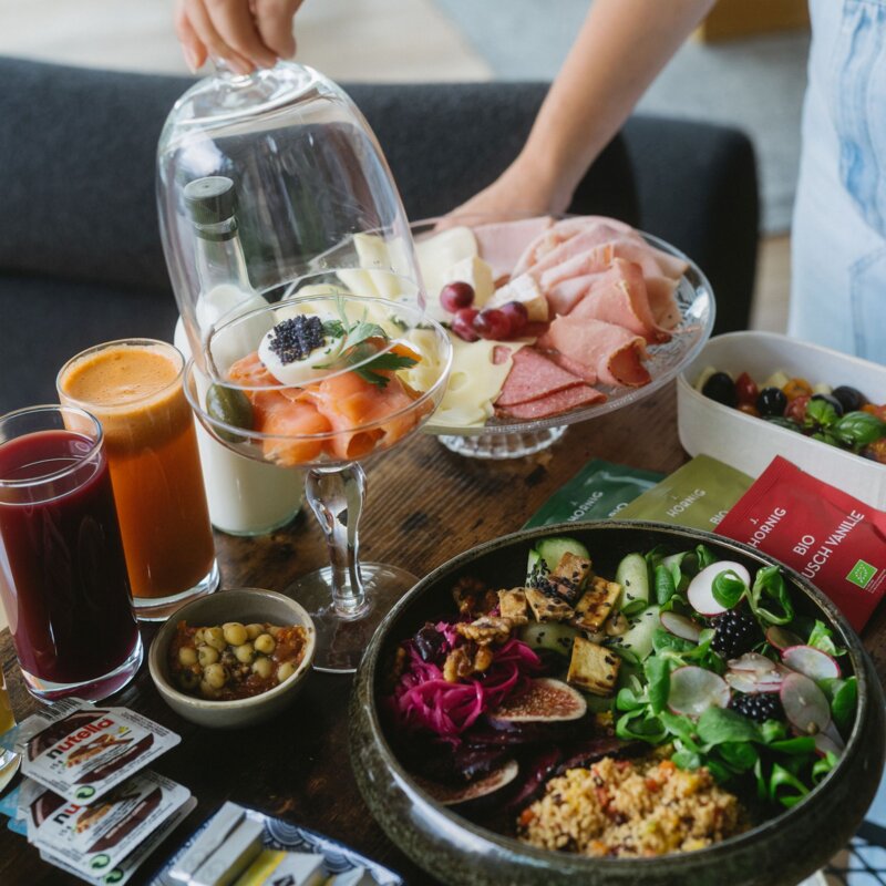 Hands arranging a brunch spread with fruit, cheese and meats.