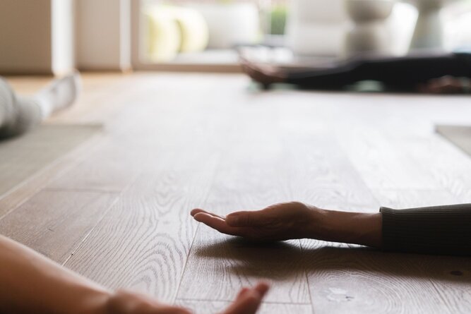 Two hands reach toward each other on a wooden floor indoors.