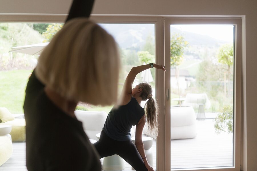 Blurred foreground observer watches person doing yoga by glass doors