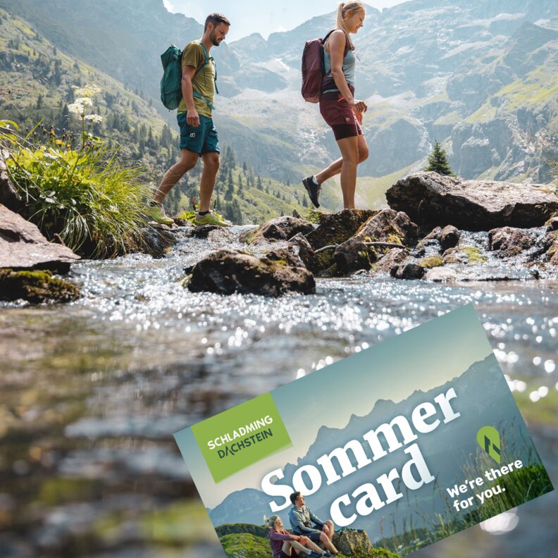 Two hikers cross a rocky stream in alpine valley; Sommer card overlay.
